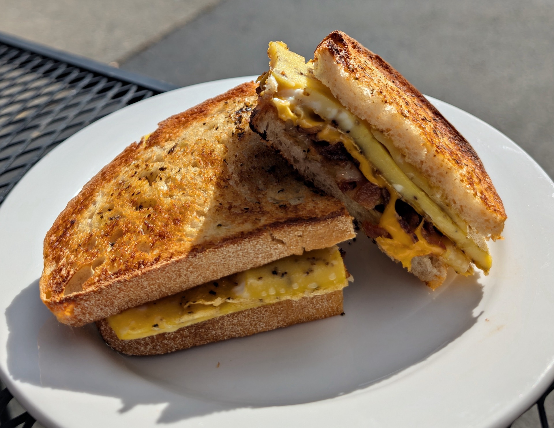 An egg, cheese and sausage sandwich on griddled sourdough, on a patio table in the sun