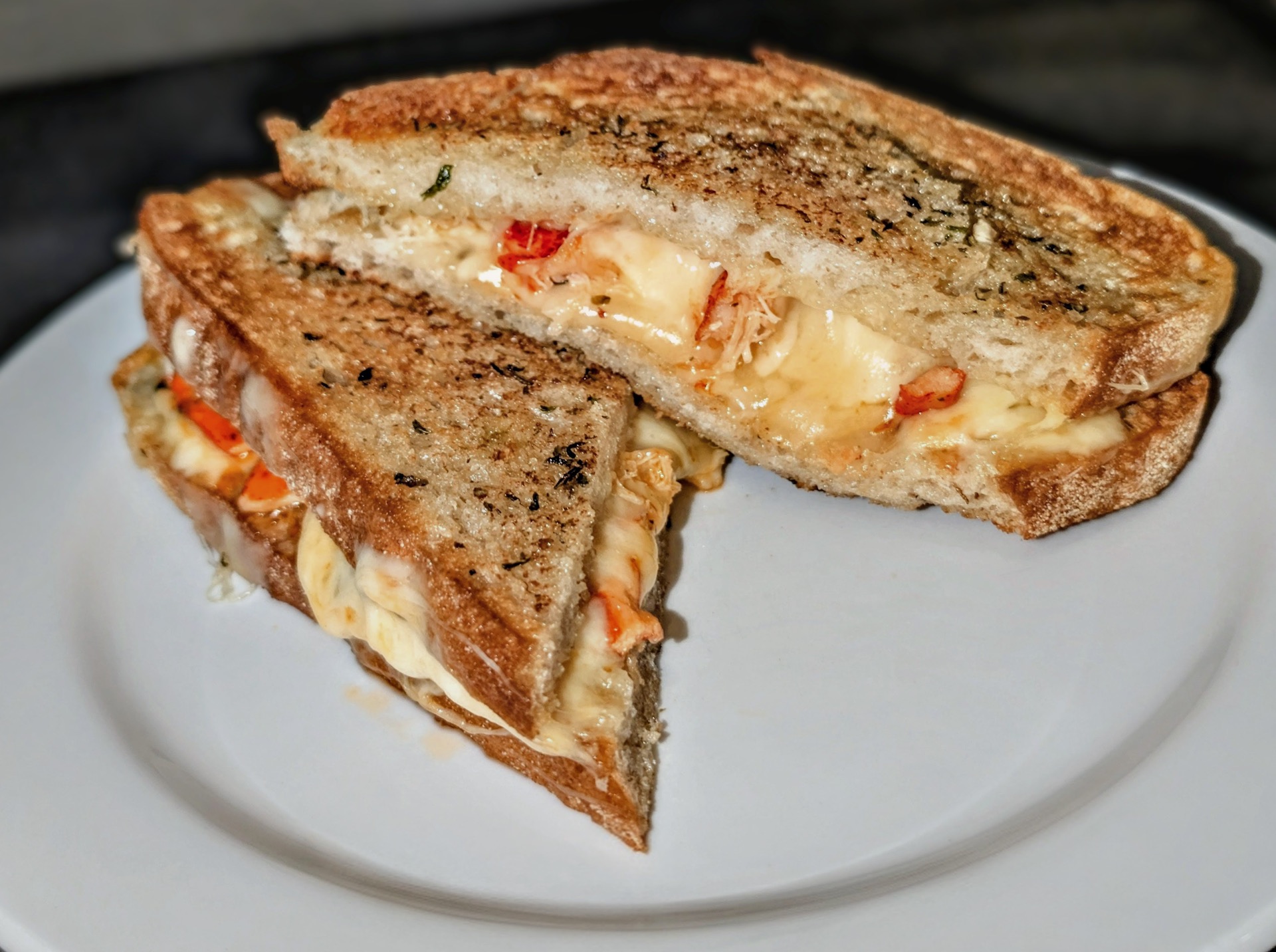 A griddled sourdough melt cut in half, with melted cheese and pieces of lobster