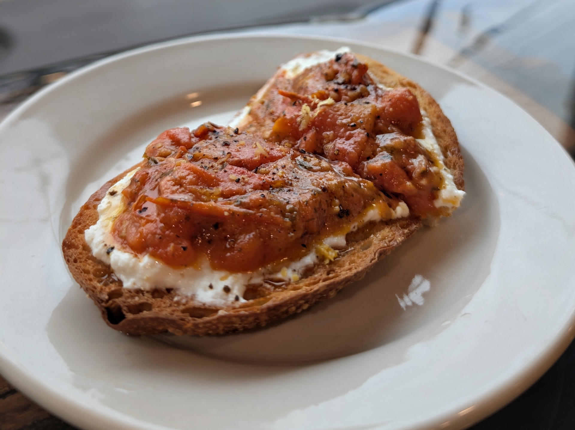 Toasted sourdough spread with whipped ricotta and topped with tomato confit and cracked pepper