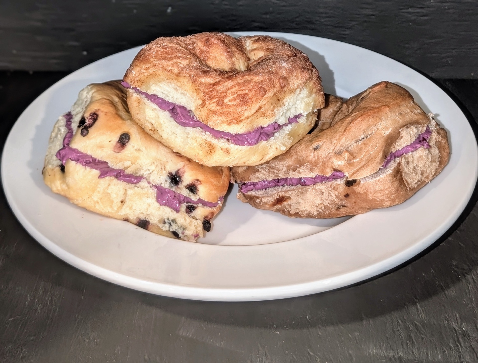 Three toasted bagels spread with purple blueberry honey cream cheese on a white plate